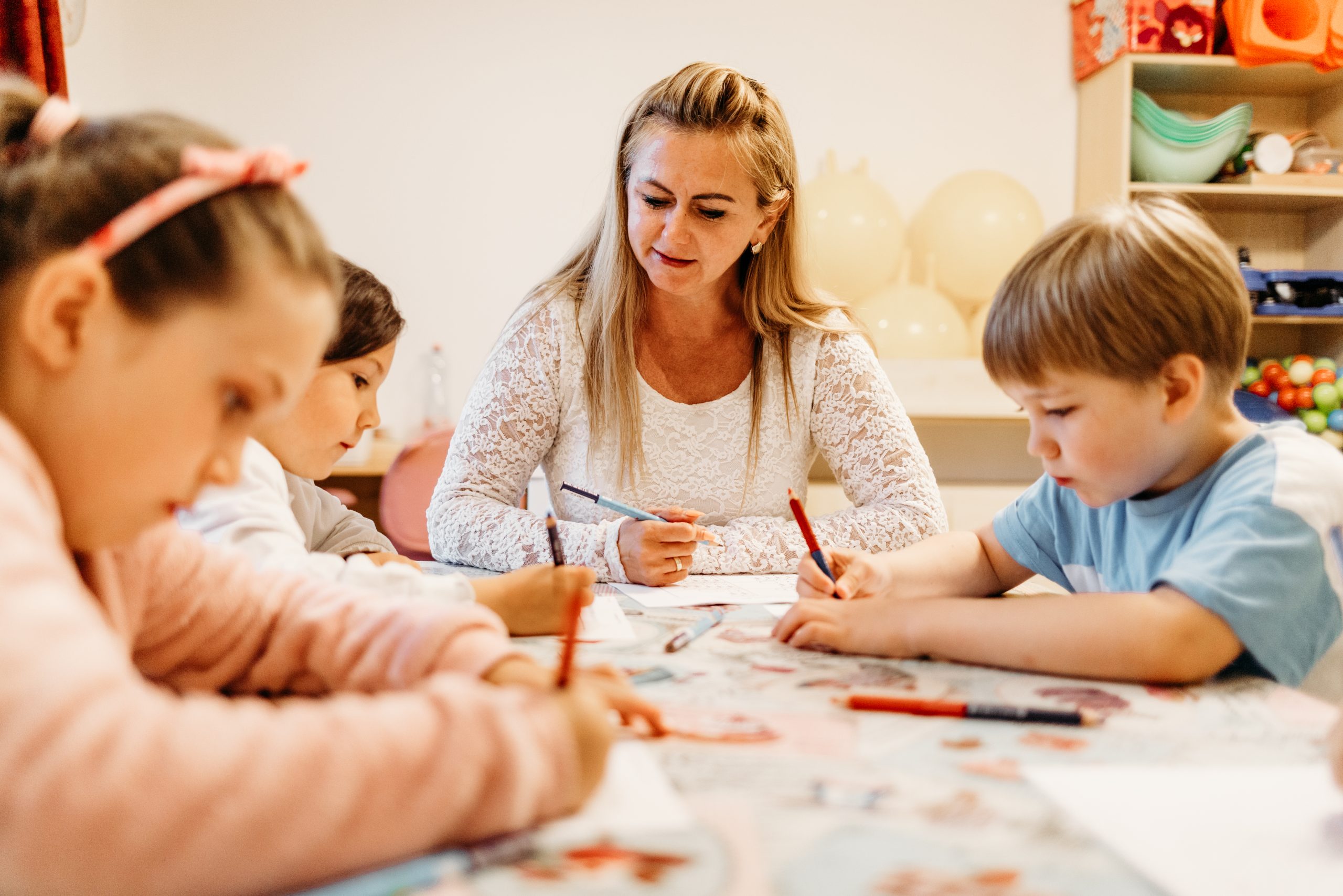 Fejlesztő szakember négy gyermekkel egy asztalnál, ahol színes ceruzával feladatlapot töltenek